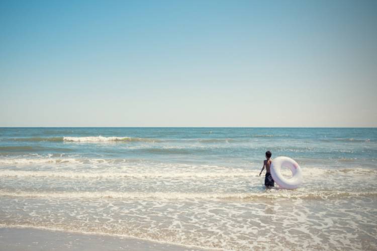 little boy with inflatable tube plays in the surf at the beach